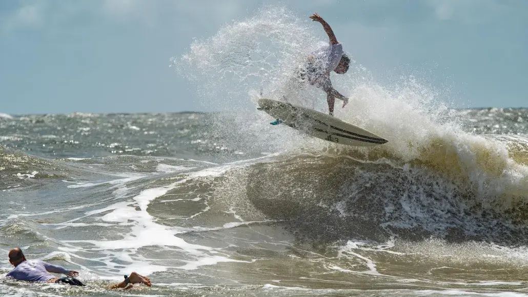 Surfer riding a breaking wave while another surfer paddles nearby.
