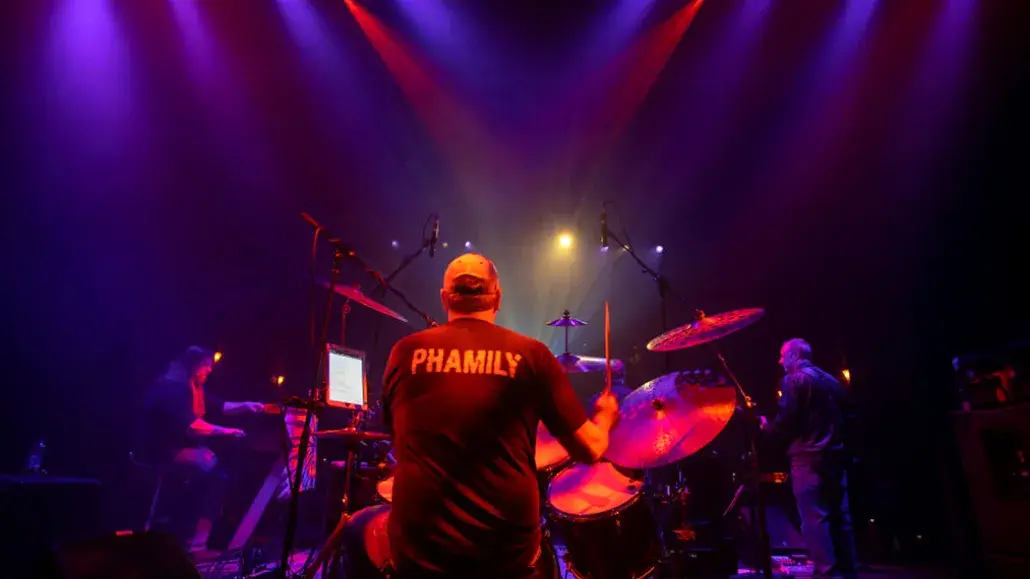 Drummer performs onstage with a band under colorful purple and red lights at the Tybee Post Theater.