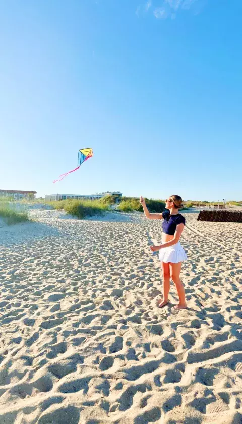A woman on the beach flying a kite.