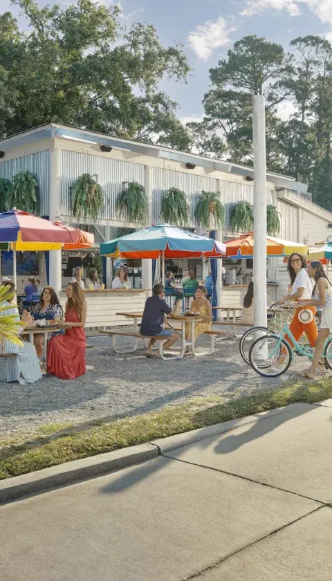People eating outdoors at a restaurant with colorful rainbow umbrellas.