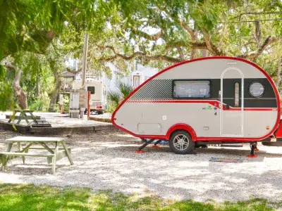 A red and white RV camper parked at a campground next to a wooden picnic table.
