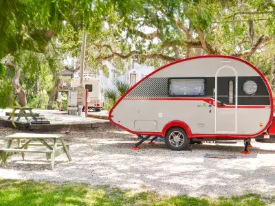 A red and white RV camper parked at a campground next to a wooden picnic table.