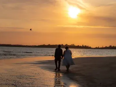 A couple holding hands while walking on the beach at sunset.