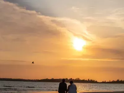 A couple holding hands while walking on the beach at sunset.