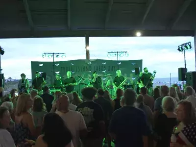 An outdoor concert with a huge crowd gathered around a stage of musicians