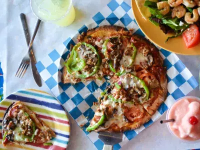 A pizza, shrimp salad and drink on a table.