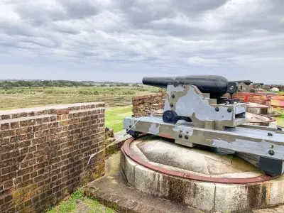 Historic cannon positioned atop Fort Pulaski’s brick ramparts, overlooking grassy coastal landscape under a cloudy sky.