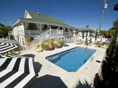Exterior view of a multi-story home with a backyard pool and multiple yellow pool chairs and black and white umbrellas.