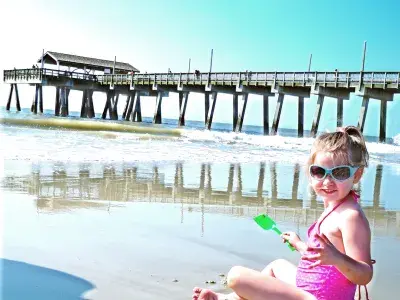 Young girl sitting and smiling on the beach with the pier in the background