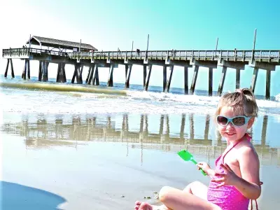 Young girl sitting and smiling on the beach with the pier in the background