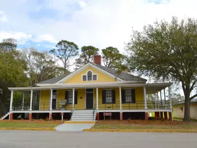 A front entrance outdoor view of a yellow historic guard house.