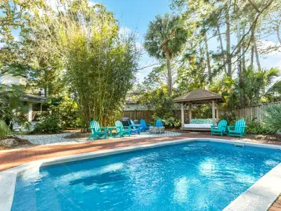A fenced in outdoor pool with multiple blue pool chairs, a pergola covered couch.