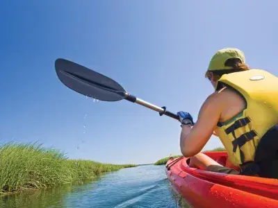 A person wearing a yellow life vest kayaking through a marsh.