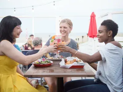 Friends cheersing while dining outdoors at a beachfront restaurant.