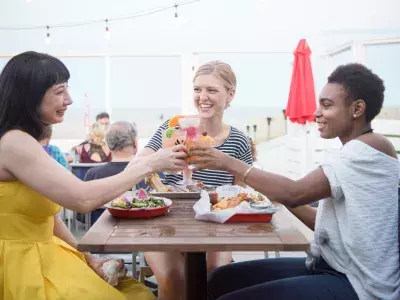 Friends cheersing while dining outdoors at a beachfront restaurant.