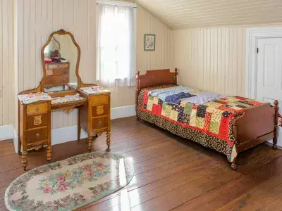 A bedroom with a twin bed, old quilt and vintage vanity