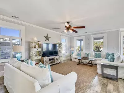 A living with white furnishings and a tv surrounded by windows.