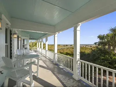 Covered balcony with seating and view of the dock to the beach