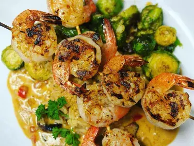 A plate of skewered shrimp with brussel sprouts.