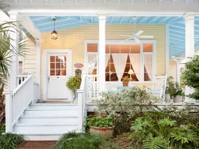 Front porch of a yellow cottage with white trim, greenery, and cozy outdoor seating.