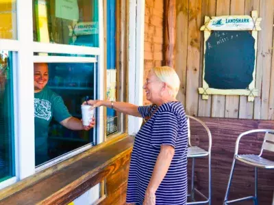 A woman grabbing a drink at an outdoor dining window on the beach.