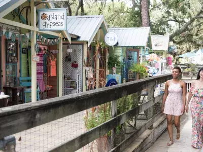 Two women strolling along a deck surrounded by different shops.
