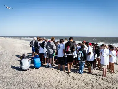 Group of students gathered on the beach listening to an instructor near the shoreline.
