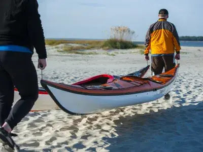 Two kayakers carrying their boat toward the ocean.
