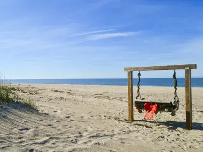A wooden swing on the beach decorated in garlands and a red bow.