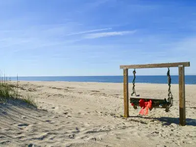 A wooden swing on the beach decorated in garlands and a red bow.