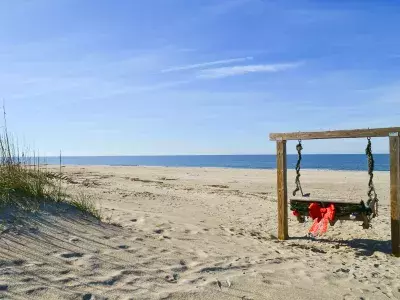 A wooden swing on the beach decorated in garlands and a red bow.