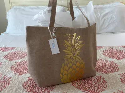 A tote bag with a gold pineapple on the front sitting on a bed.
