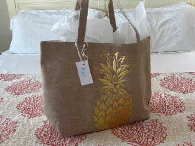 A tote bag with a gold pineapple on the front sitting on a bed.