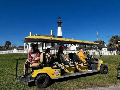 A small group on a golf cart tour with a lighthouse in the background.