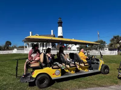 A small group on a golf cart tour with a lighthouse in the background.