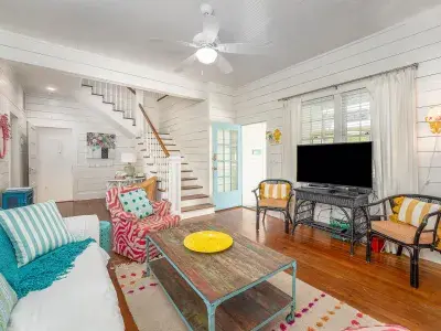 A spacious family room with colorful decor, ample seating and view of a white staircase.