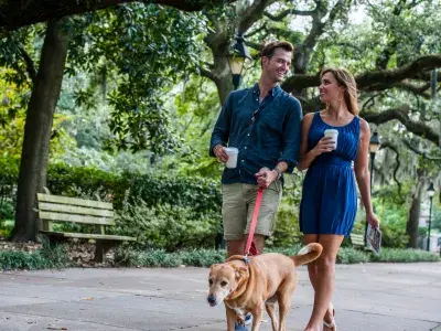Couple walking their dog under Spanish moss-draped oaks in Savannah’s Forsyth Park, enjoying coffee and a peaceful stroll together.