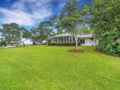 Exterior view of Horsepen Cottage by Coastline Concierge, set on a wide waterfront lawn with live oaks and marsh views.