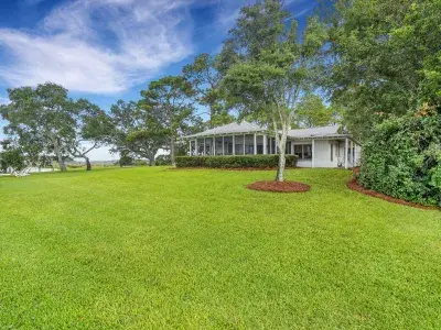 Exterior view of Horsepen Cottage by Coastline Concierge, set on a wide waterfront lawn with live oaks and marsh views.