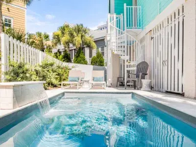 Private pool with waterfall feature at Big Wave on Tybee Island, surrounded by coastal homes, palm trees and lounge seating.
