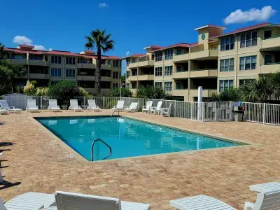 Community pool at Tybee Island condo complex with lounge chairs, palm trees and surrounding multi-story buildings.
