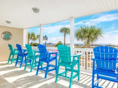 Covered balcony at Dolphin Watch featuring colorful Adirondack chairs overlooking palm trees and ocean views.