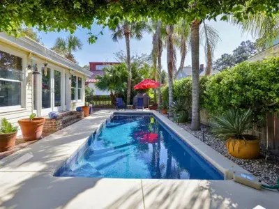 Private backyard pool at Island Bliss on Tybee Island, surrounded by palm trees, lush greenery and shaded patio seating.