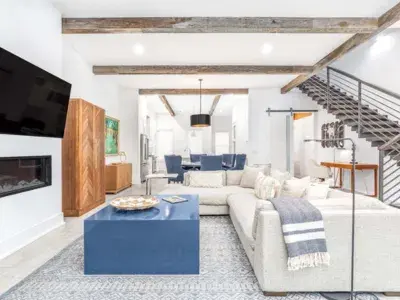Modern coastal living room at Savannah Jetsetter featuring exposed wood beams, neutral seating, blue accent table and open-concept layout.