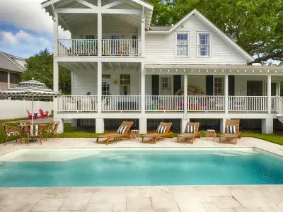 Historic Bliss Cottage on Tybee Island featuring wraparound porches, white coastal architecture, lounge chairs and a private saltwater pool.