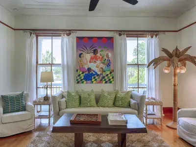 Bright living room inside Officer’s Row featuring colorful artwork, tall windows, vintage architectural details, white seating and coastal-inspired décor.