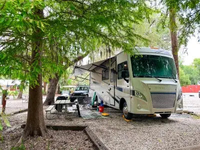 RV parked at a shaded campsite beneath mature trees at River’s End Campground
