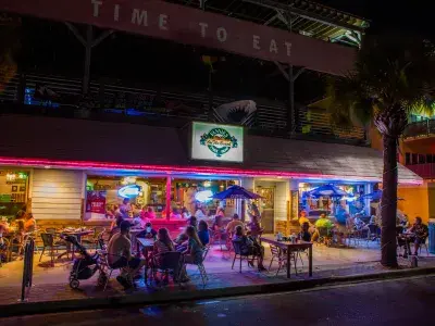 A nighttime exterior view of people eating outdoors in front of a restaurant.