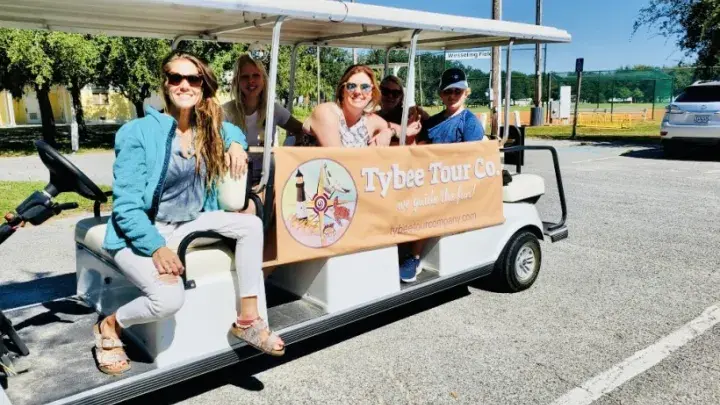A group of people sitting on a multiple row seat golf cart.