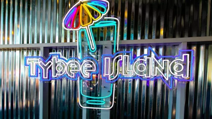 A rainbow-colored neon sign of a glass with an umbrella in it that reads Tybee Island.